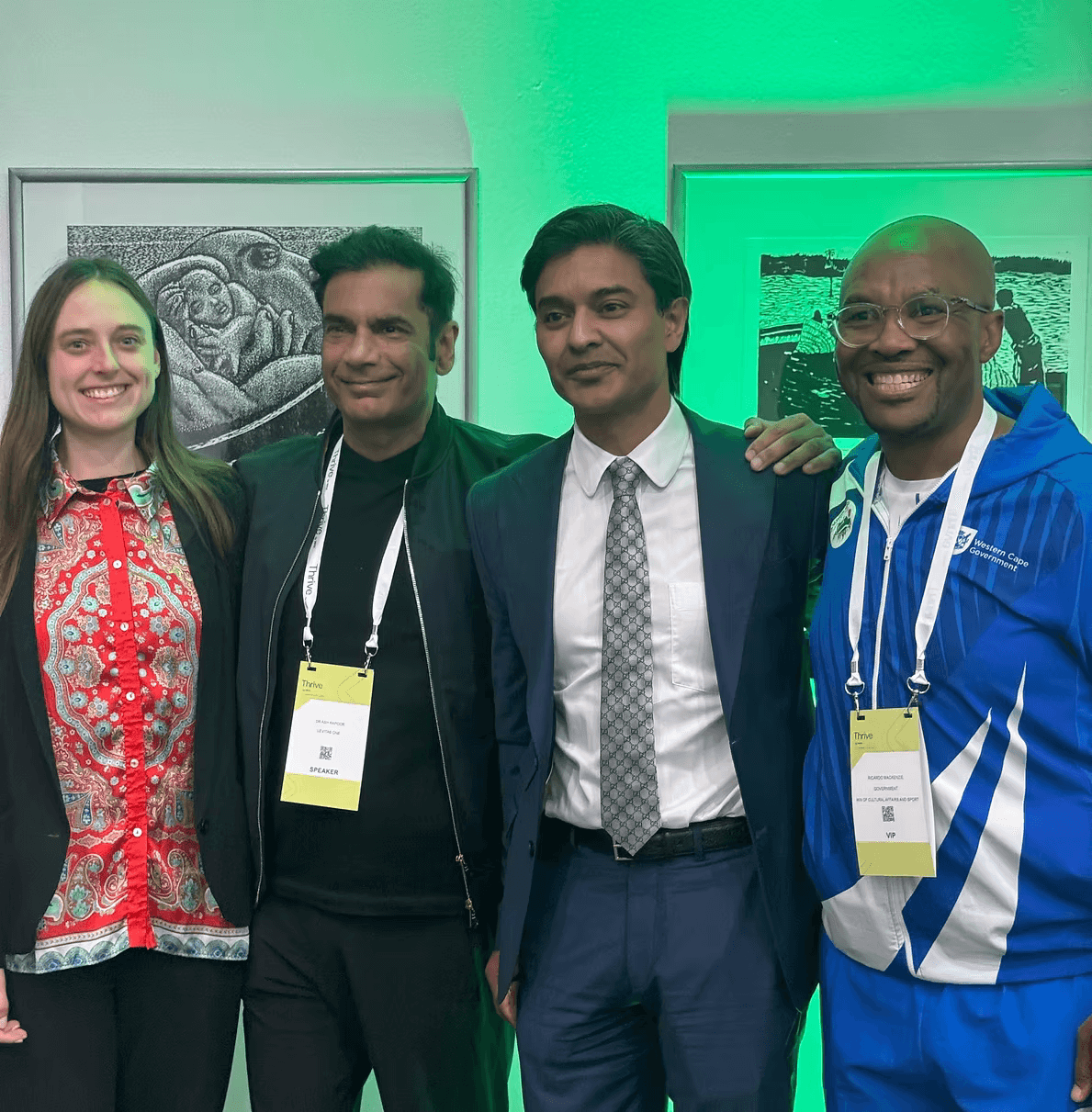Four people smiling together under green lighting at the Thrive summit in Cape Town, in front of framed black-and-white prints, two of them wearing speaker and VIP badges